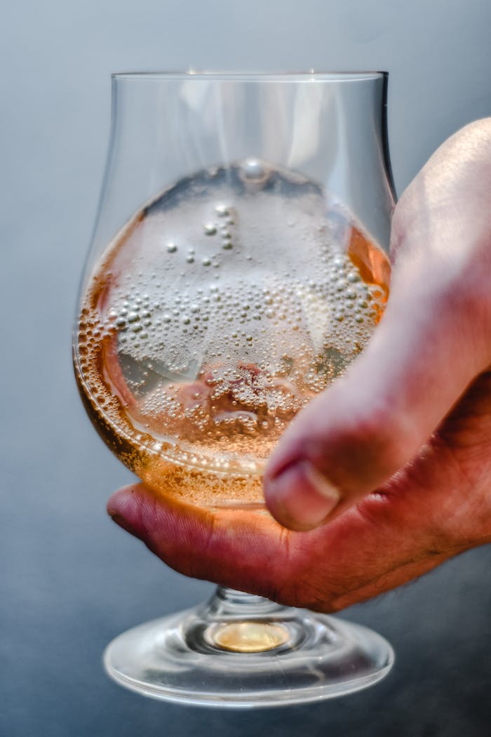 Detailed view of a hand holding a glass of sparkling lager beer, showcasing bubbles and amber hue.